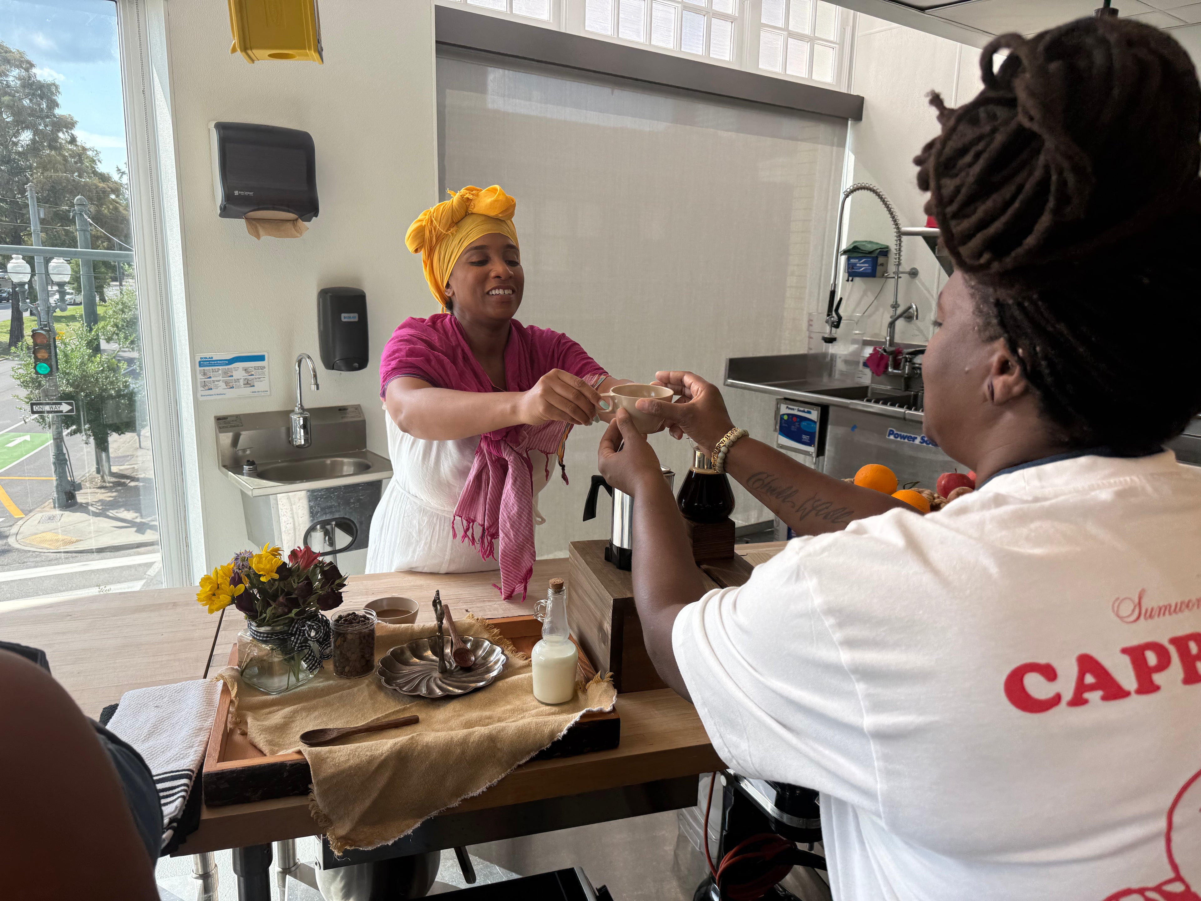 Rose Nicaud (Queen Shereen) interacting with guest at a coffee tasting   with New Orleans street scene. 