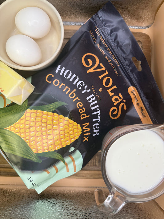 O'Violas Honey Butter Cornbread Mix package with eggs, butter, and a measuring cup on a wooden surface.